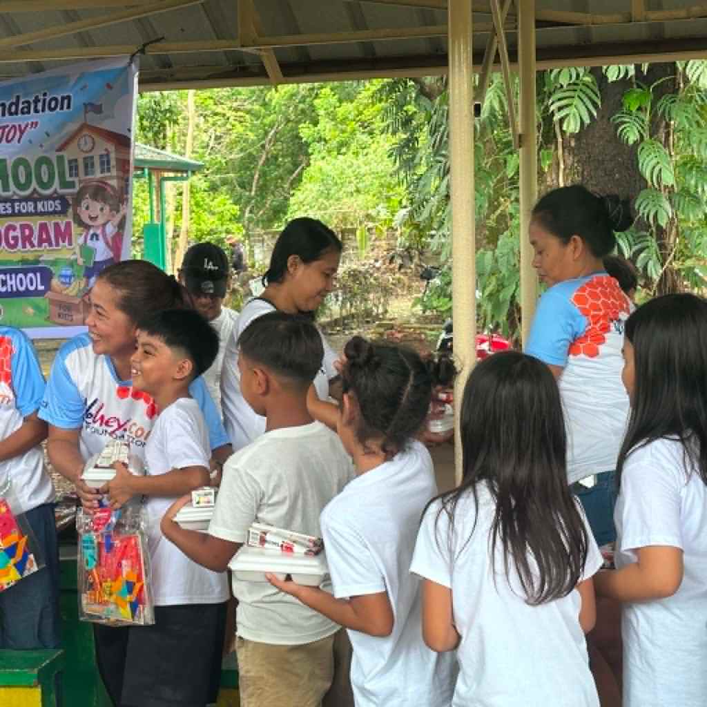 A group of children and adults participating in a community program, engaged in an activity with educational materials in a green outdoor setting.