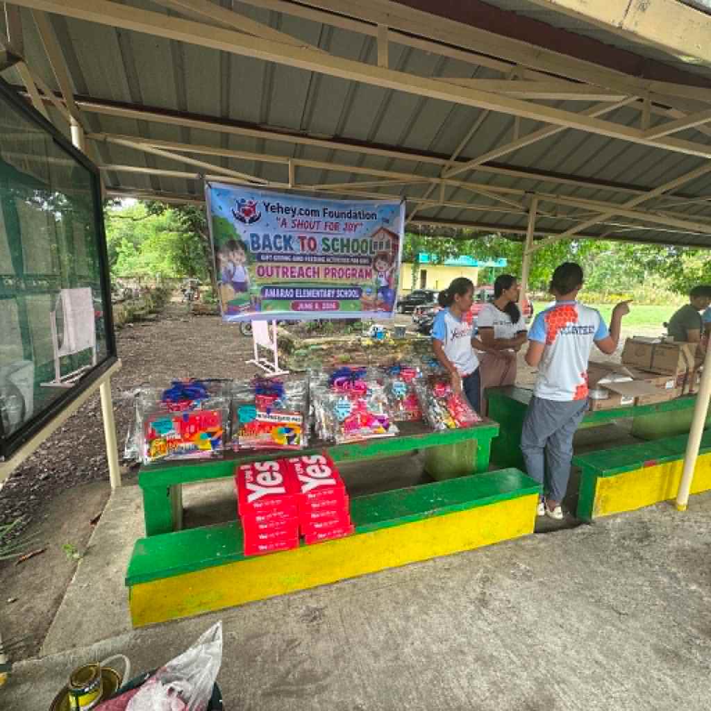 A community outreach program booth for the 'Back to School' initiative hosted by Yehey.com Foundation at Amarao Elementary School, featuring colorful school supplies and volunteers assisting children.