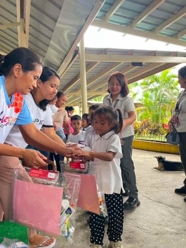 Children receiving educational supplies from volunteers during a community outreach event.