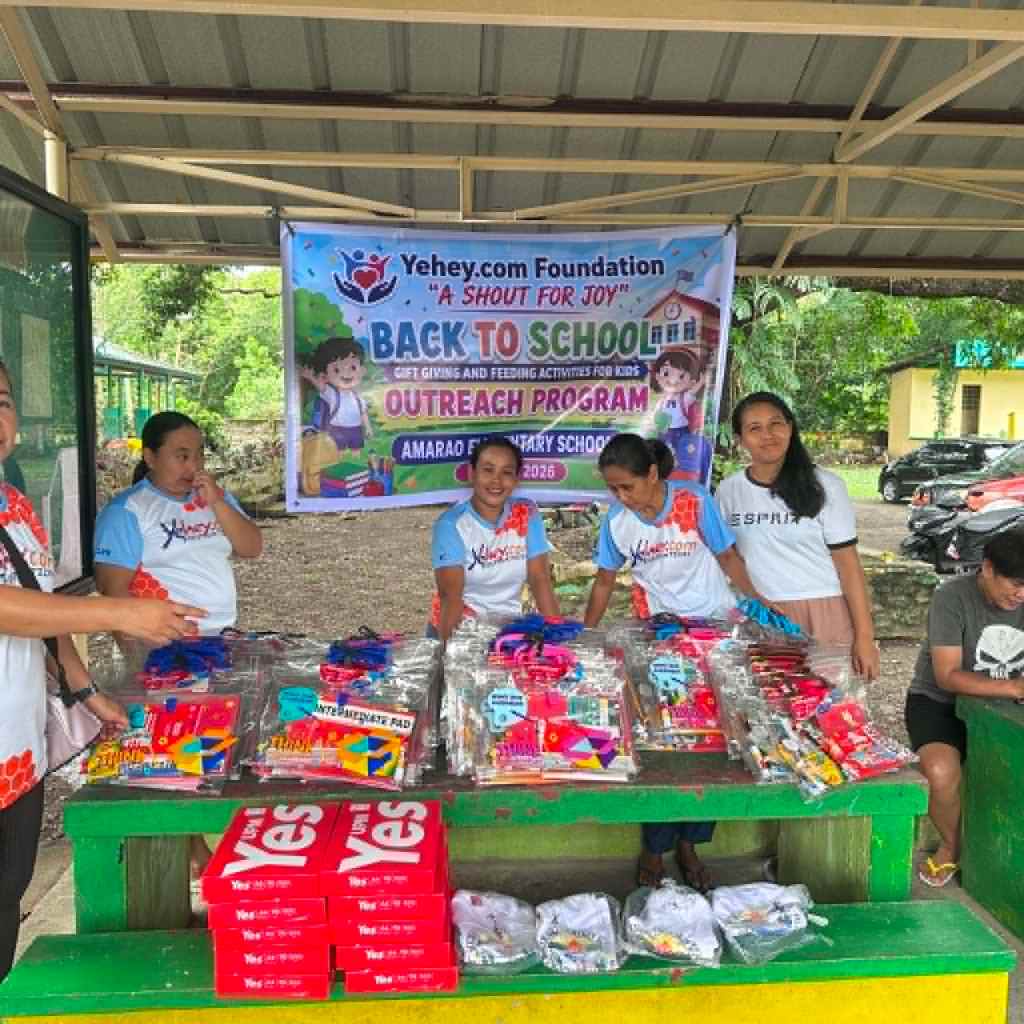Volunteers at an outreach program event organized by Yehey.com Foundation, providing school supplies and gifts for children at Amarao Elementary School. A banner promoting the 'Back to School' initiative is displayed in the background.